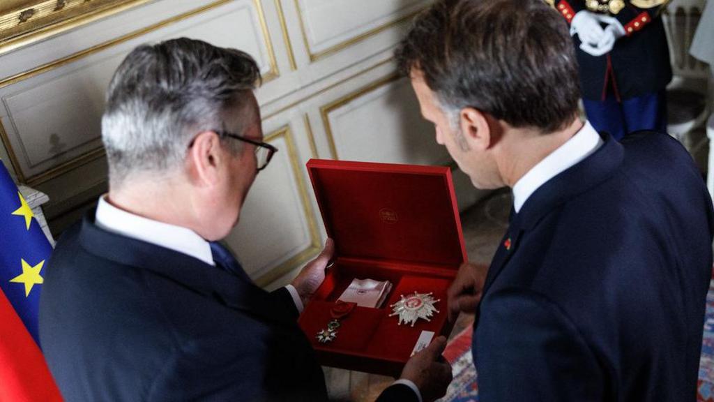 Sir Keir Starmer and Emmanuel Macron pictured from behind as they look at the opened red-velvet box Starmer is holding in his hands with the decoration visible inside