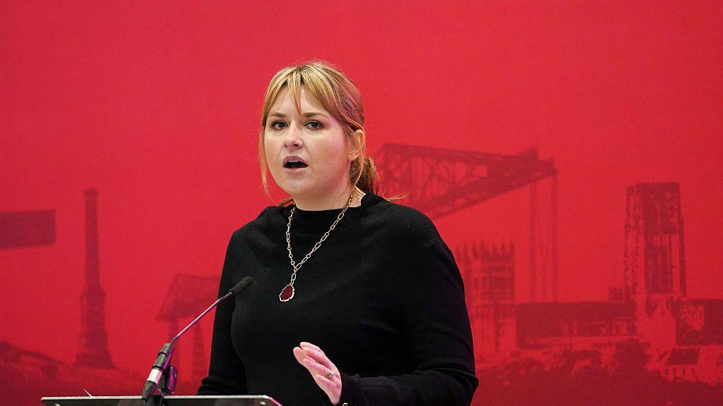Labour general secretary Hollie Ridley making a speech. She is wearing a black dress with a necklace.