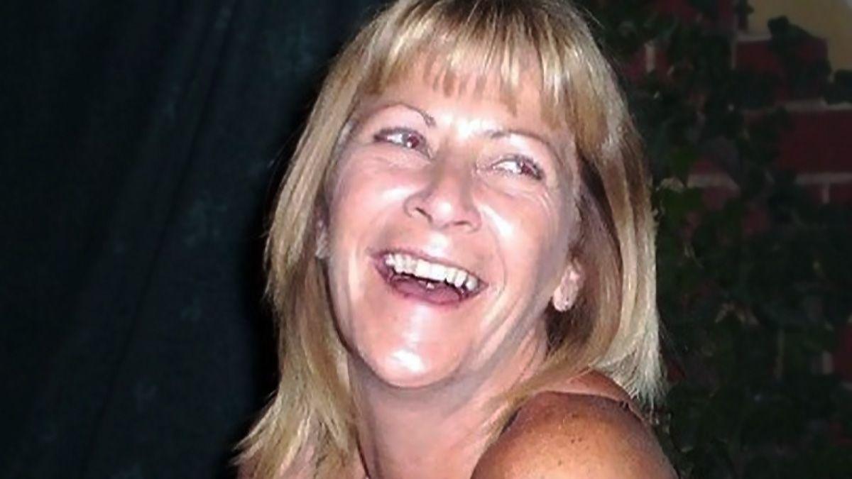 Jean Hanlon looking slightly off camera. She has shoulder-length blonde hair and is laughing. Her top row of teeth are visible. She has light-coloured eyes. Only her shoulders, neck and head can be seen.