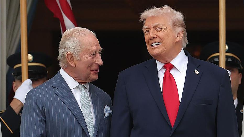 King Charles looking at Donald Trump, both wearing suits and smiling.