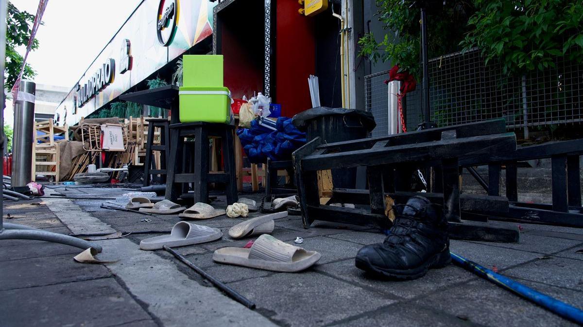 Pairs of slightly charred slippers strewn on a street outside the bar, with high stools in the background.