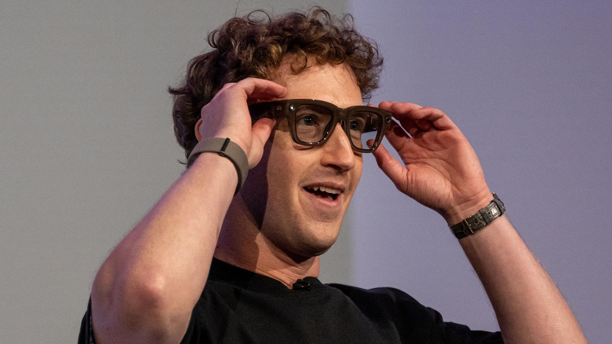 A curly haired man in a dark shirt models a pair of heavy framed glasses