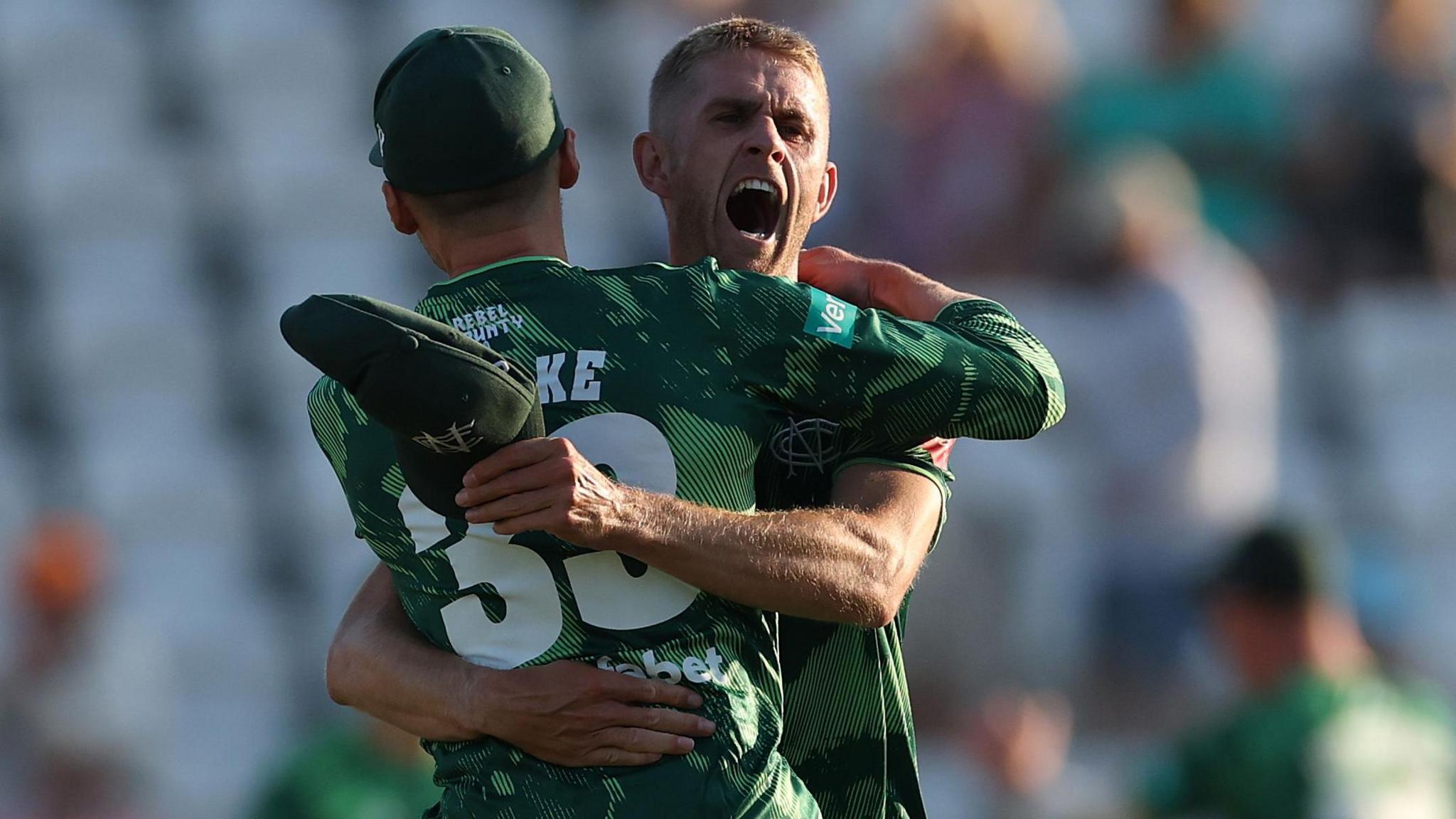 Olly Stone, wearing the green Notts Outlaws jersey, celebrates after beating Surrey in a tight encounter at Trent Bridge. He can be seen shouting in celebrating while hugging Notts captain Joe Clarke.