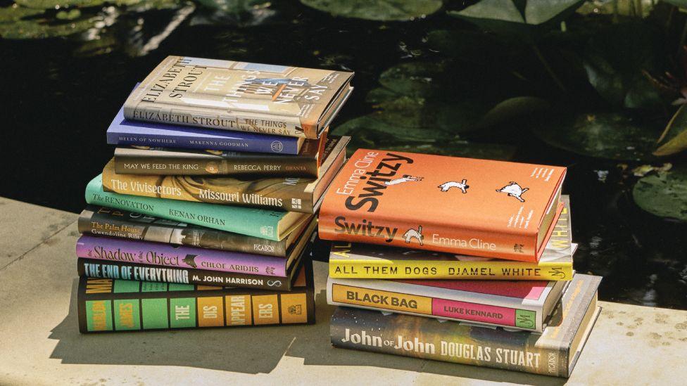 The 13 books longlisted for this year's Booker Prize, pictured on an outdoor ledge with a pond in the background