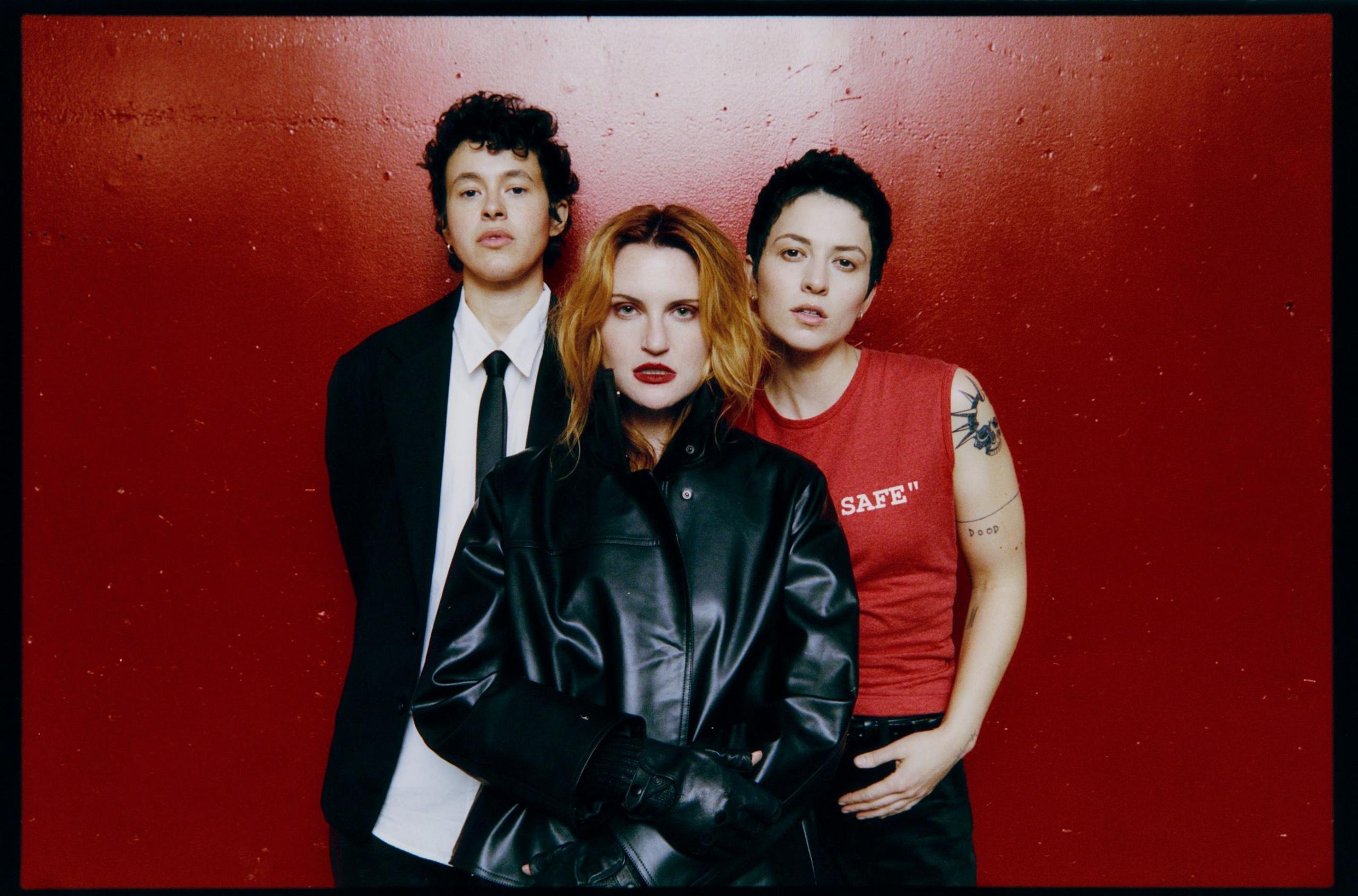 Promotional photo of Muna, standing against a blood red wall