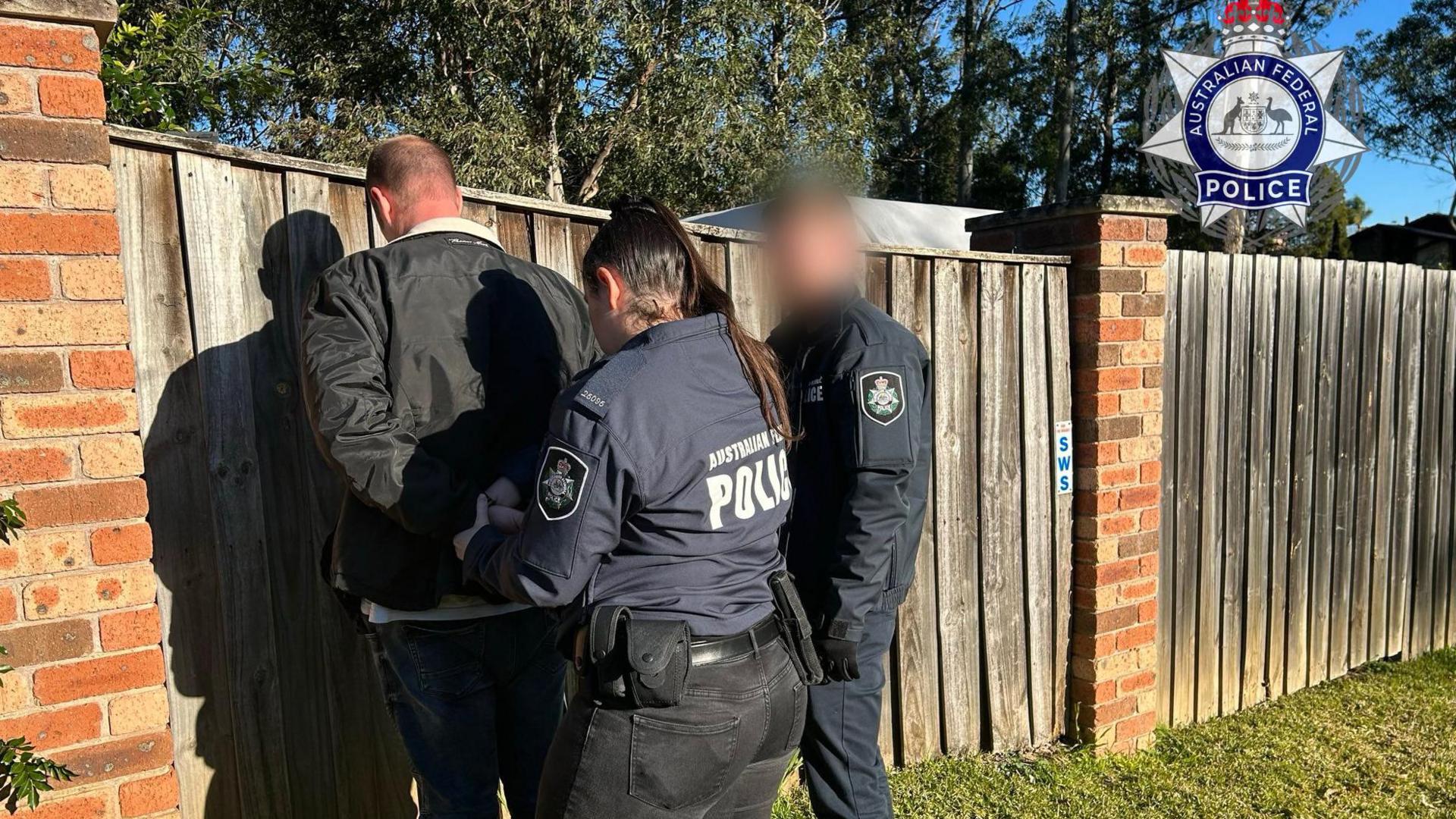 A handout photo by police shows Hamish, who can only be seen from the back, being handcuffed by police
