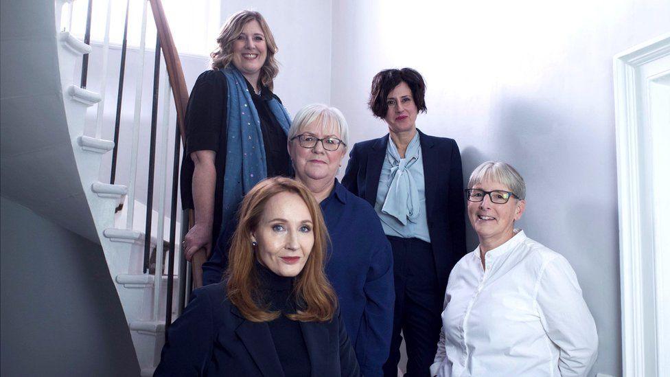 A group of women sitting on a staircase in a room with grey walls