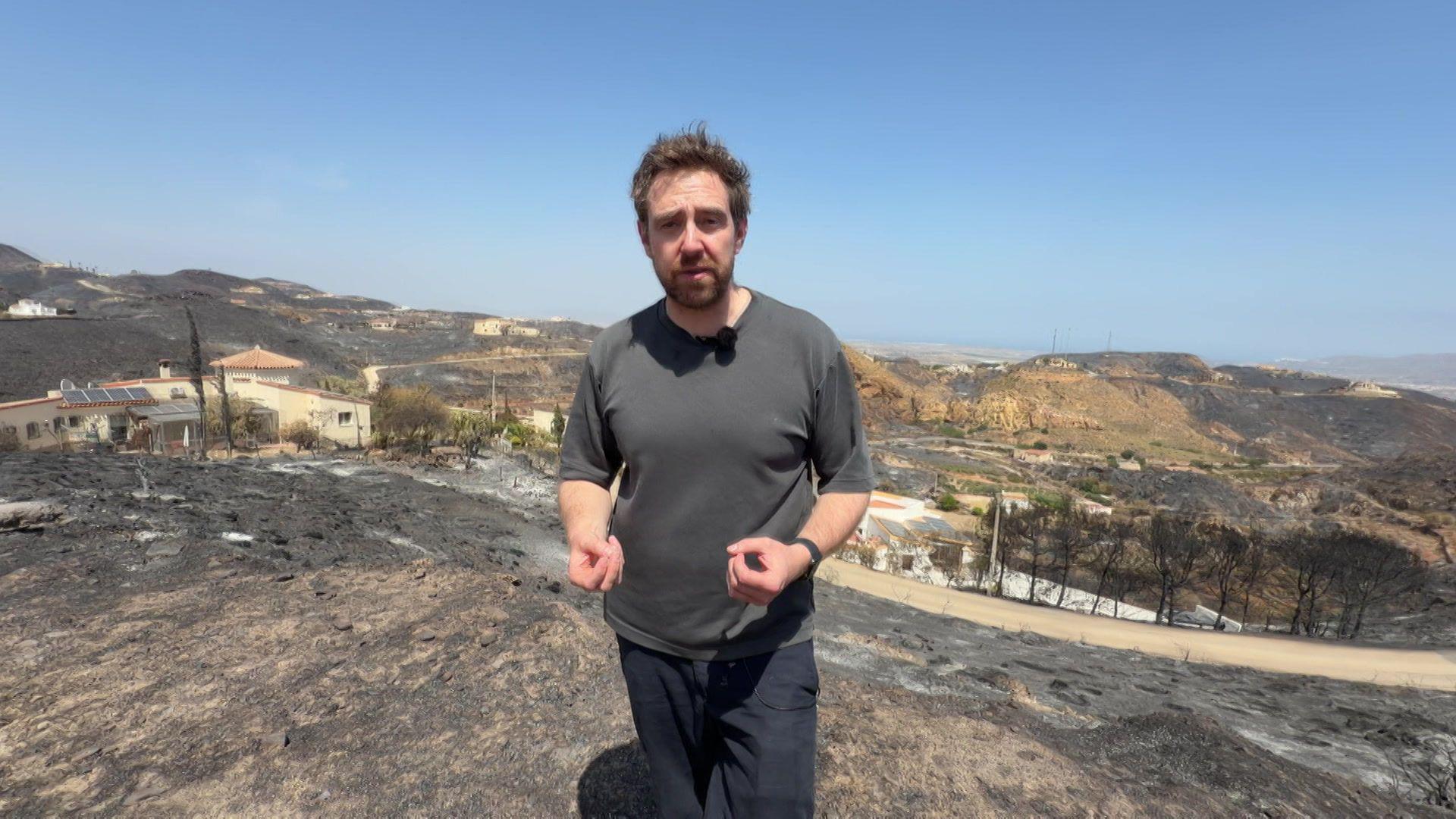 Nick Beake in a black shirt standing in the aftermath of wildfire.