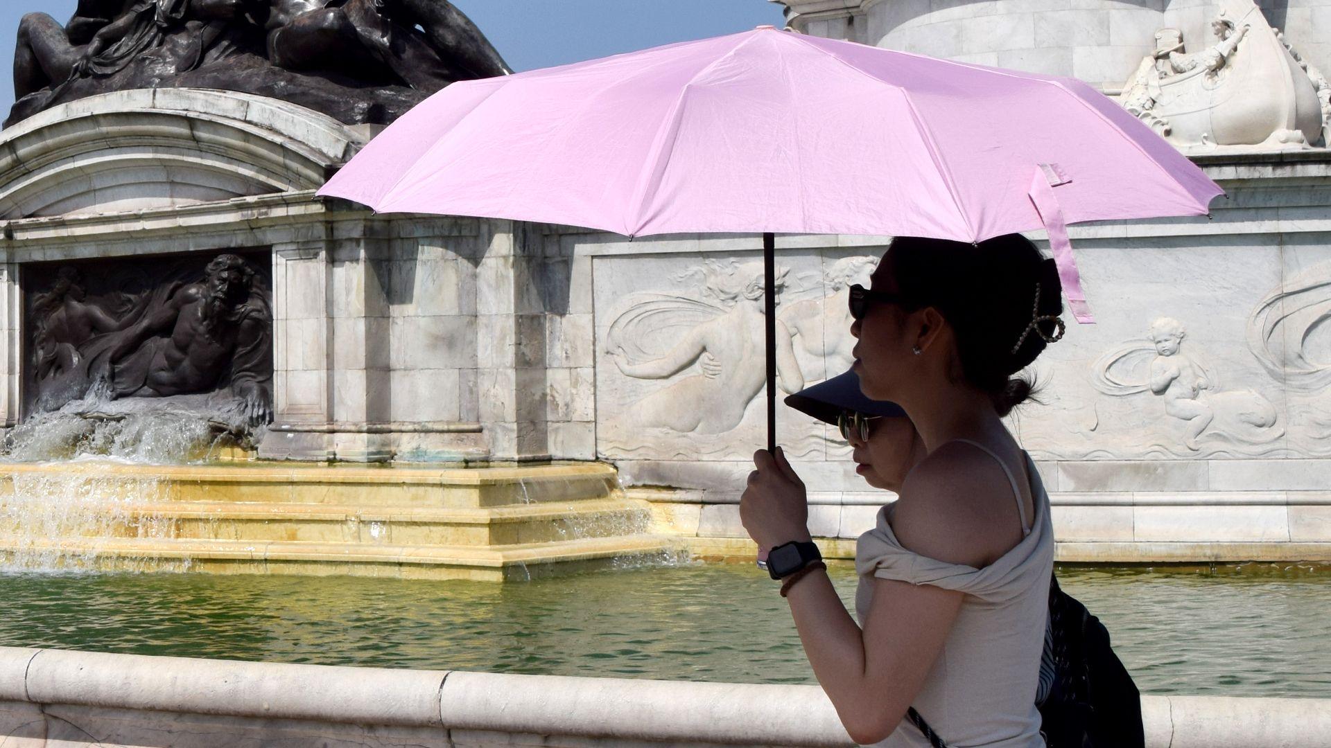 People shelter under an umbrella from the scorching sun next to the Victoria Memorial outside Buckingham Palace in London