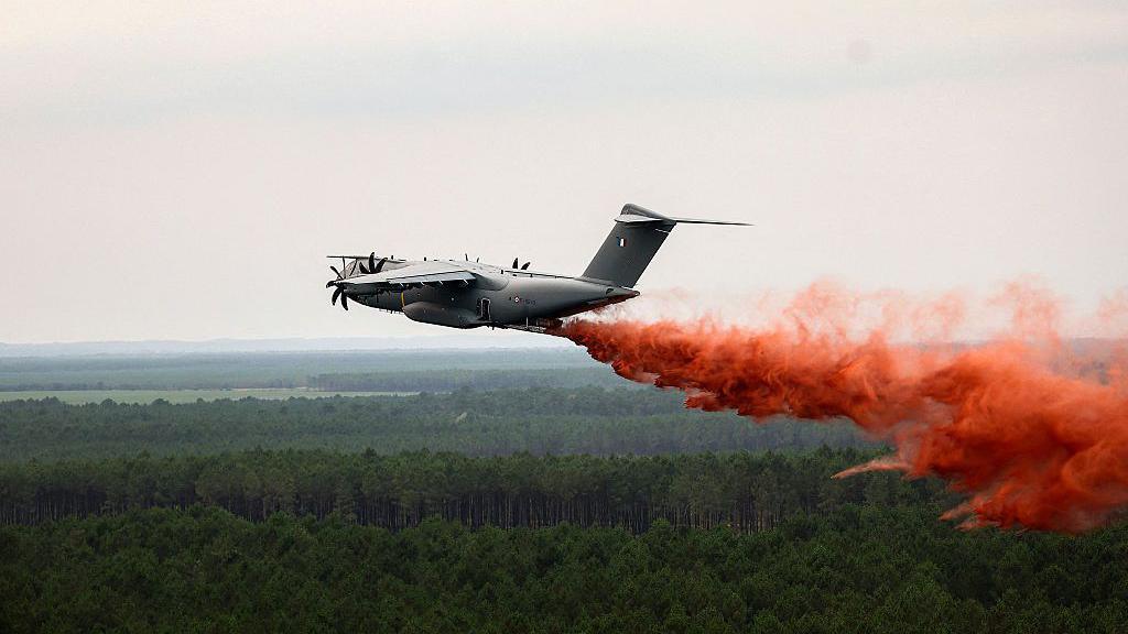 Plane drops red fire retardant over woodland.