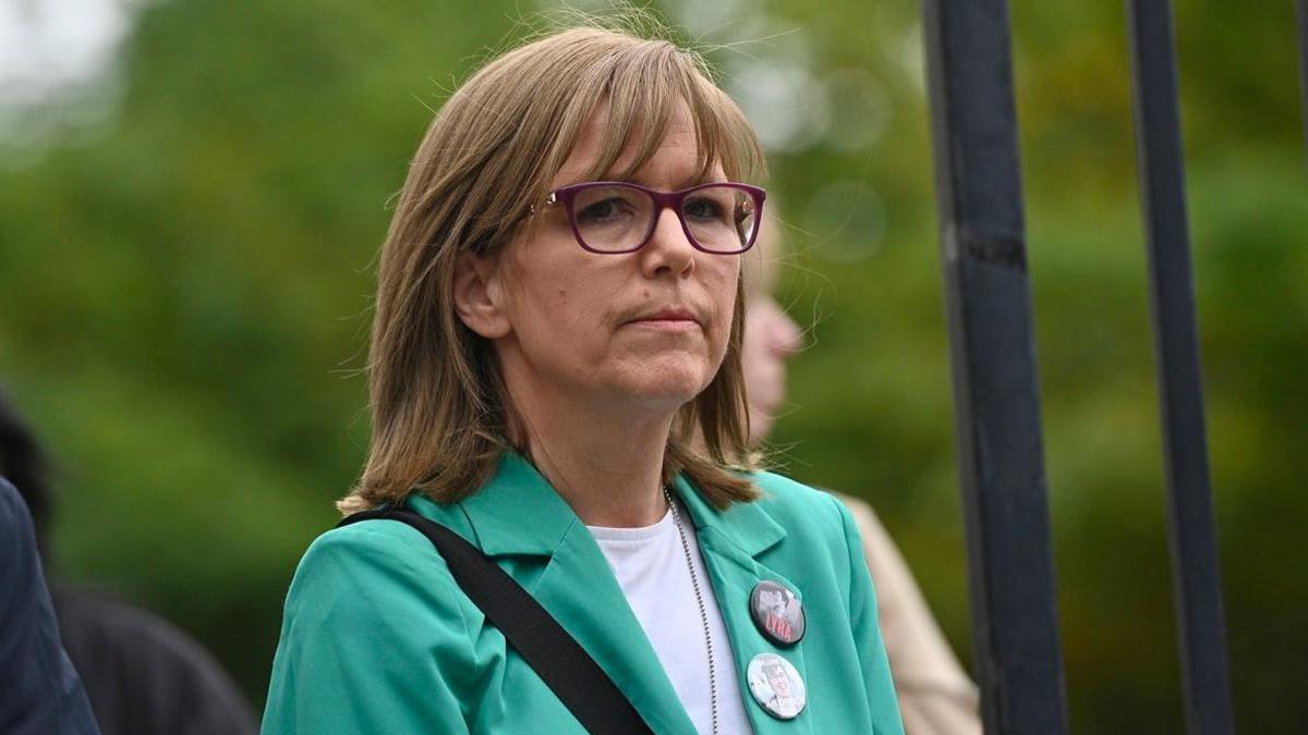 Lyra McKee's sister Nichola is wearing a green jacket and is speaking into a microphone outside court. She has sandy coloured hair and glasses.