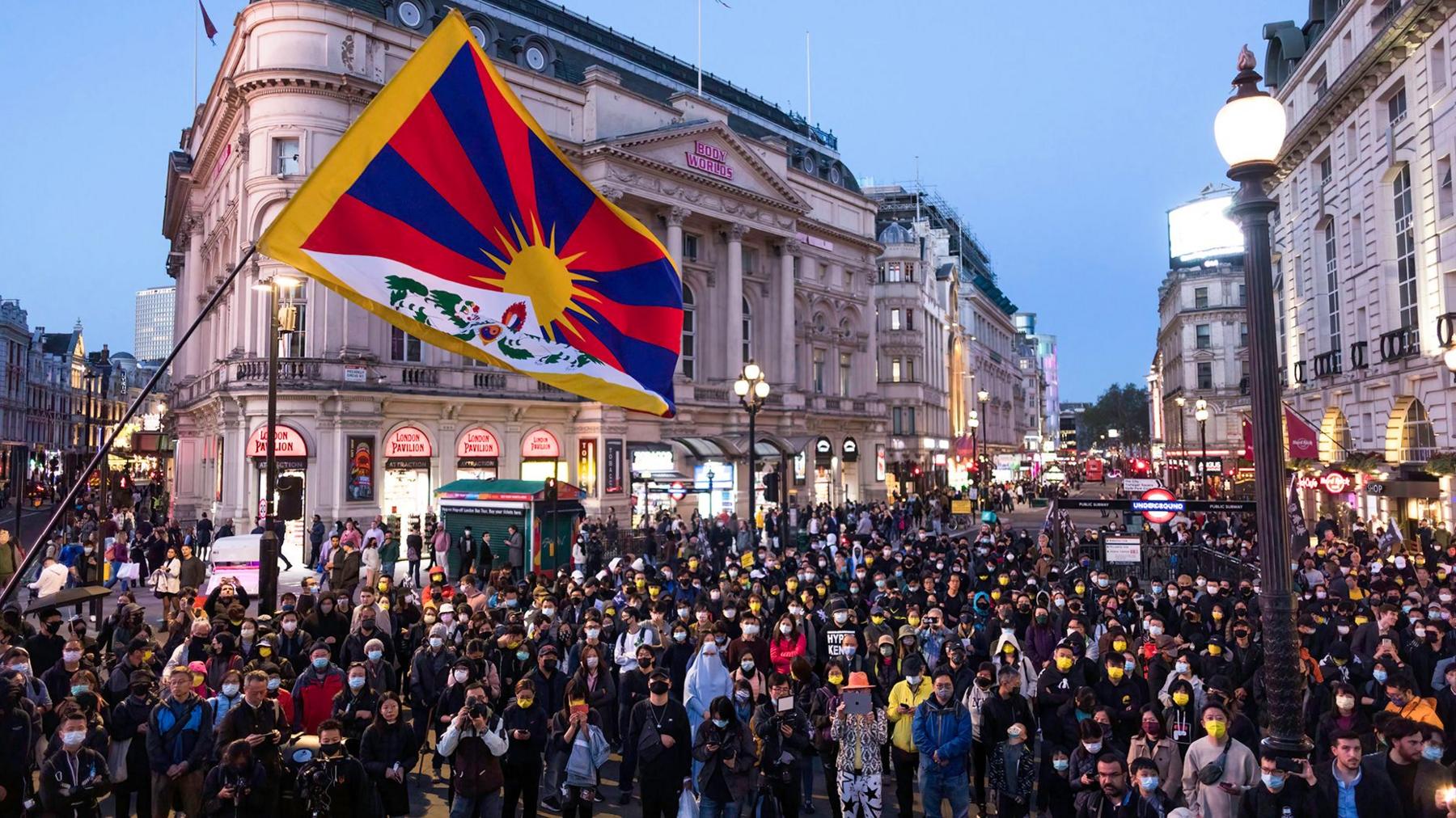 Protesters seen gathering at Piccadilly Circus during the demonstration with a Tibetan flag flying in the foreground.