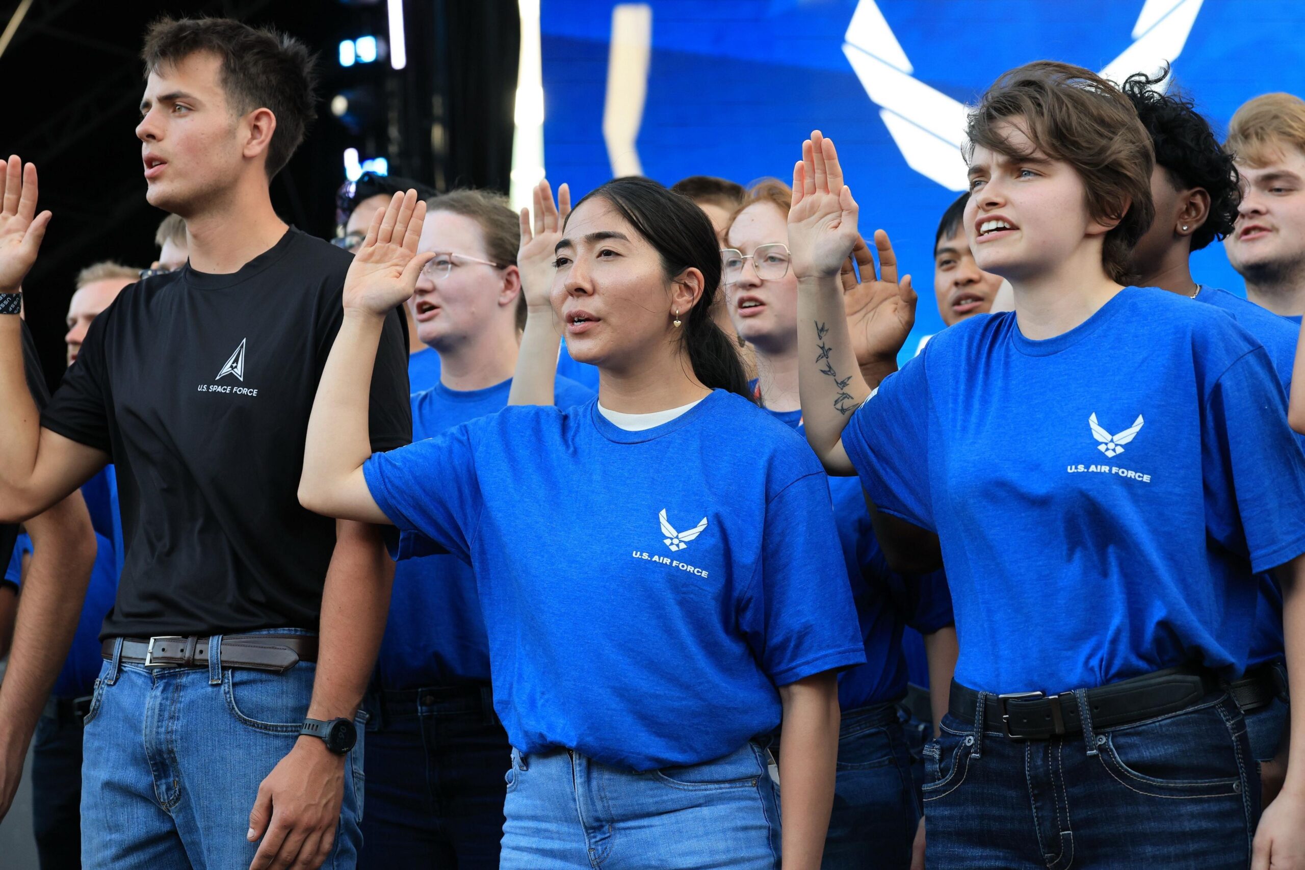 A ling of young people in blue and black Space Force logo t-shirts hold up their right hand as they take an oath