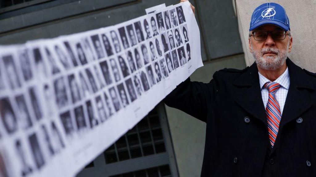 Paul Hudson, whose daughter Melina was one of the victims in the Pan Am Flight 103 Lockerbie bombing, holds up a banner of pictures of additional victims outside the federal court before the trial for a Libyan man accused of making the bomb