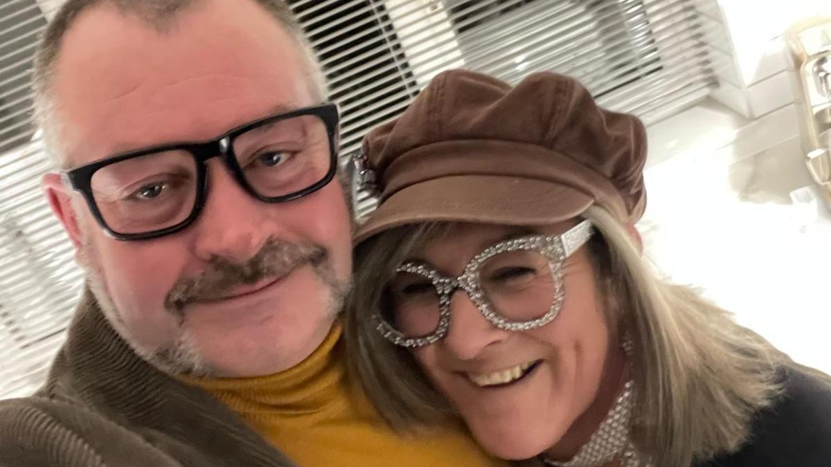David Griffiths and Helen Moorefield at a fancy dress party. Helen is laughing and wearing large, sparkly diamante glasses. Griffiths is wearing a mustard turtle-neck jumper, brown, brown corduroy jacket and dark-rimmed glasses.