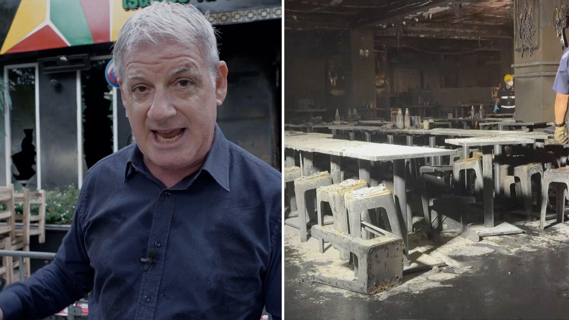A man speaking in front of a building, and on the right the inside of a burned building with tables and chairs.
