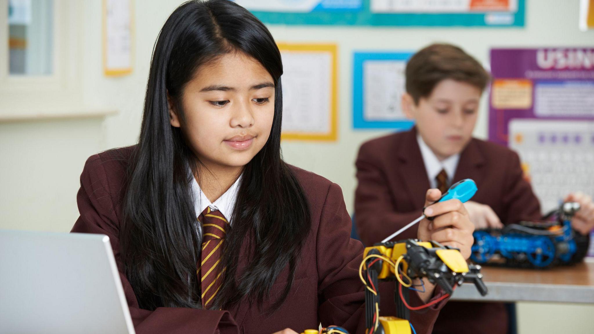 A pupil in uniform uses a tool to build a robot