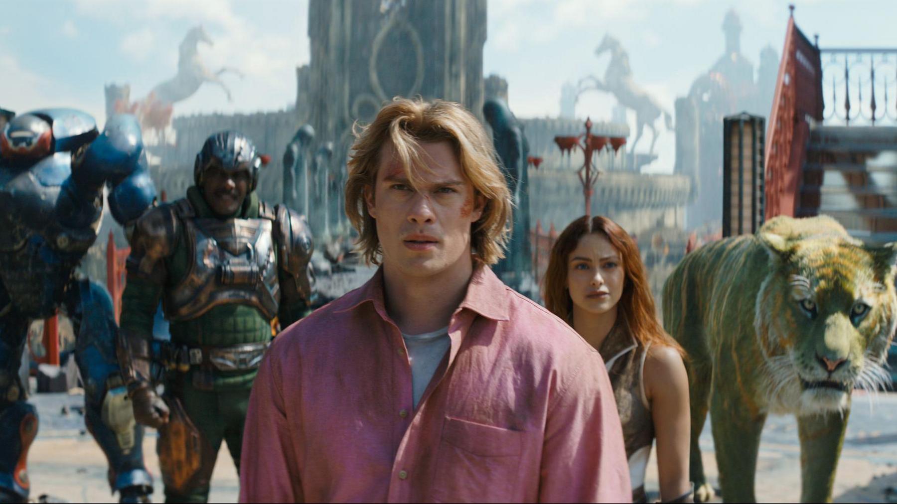 Masters of the Universe still. A group of superhero characters and a CGI lion are stood in a line in front of a tall building.