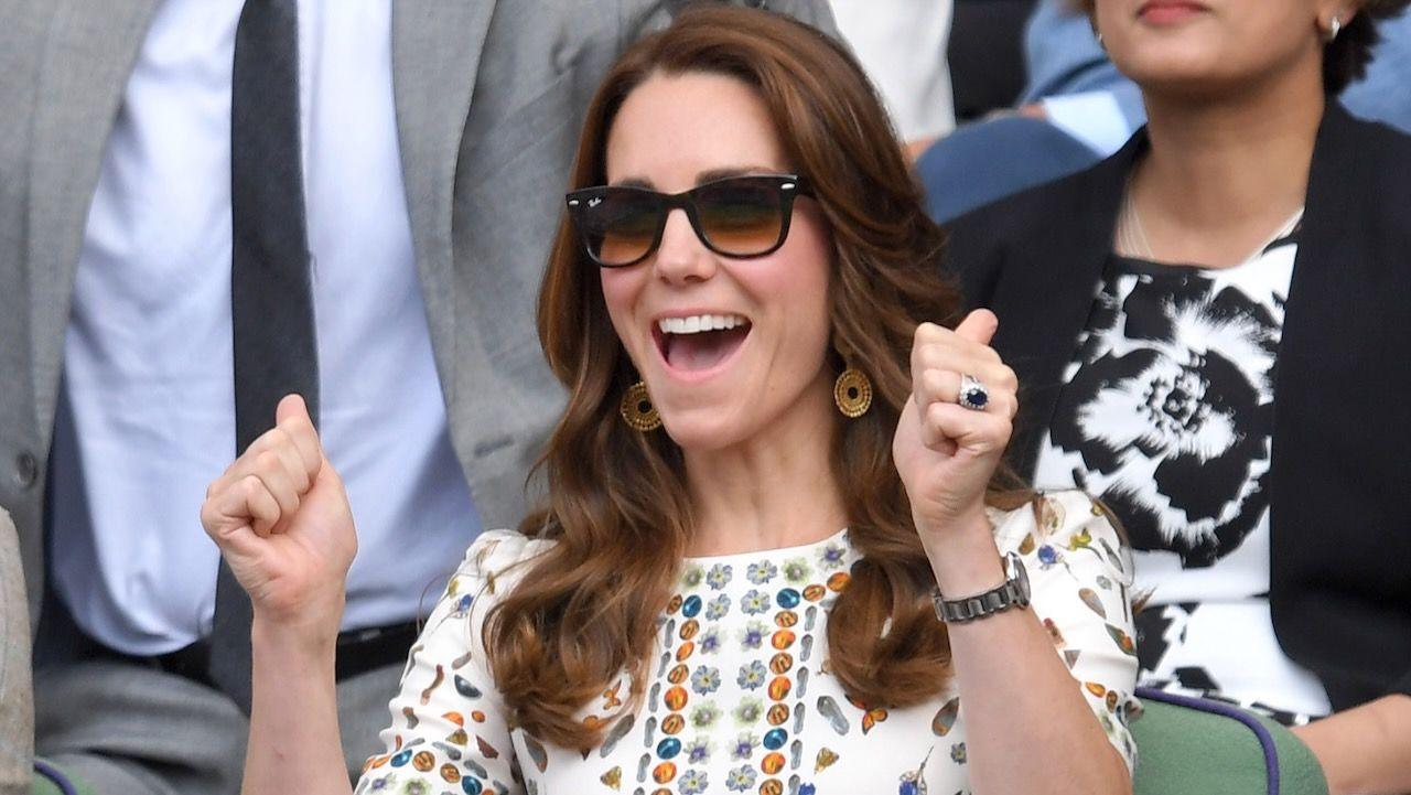 The Princess of Wales with her hands up at Wimbledon in 2016. She is wearing a white printed dress, golden earrings and sunglasses.
