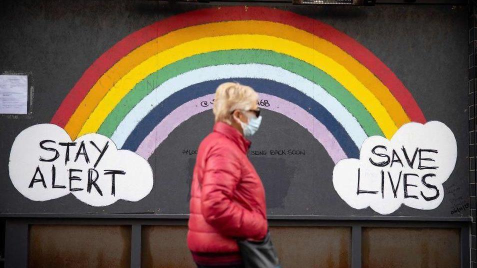 Woman walking down street past Covid sign