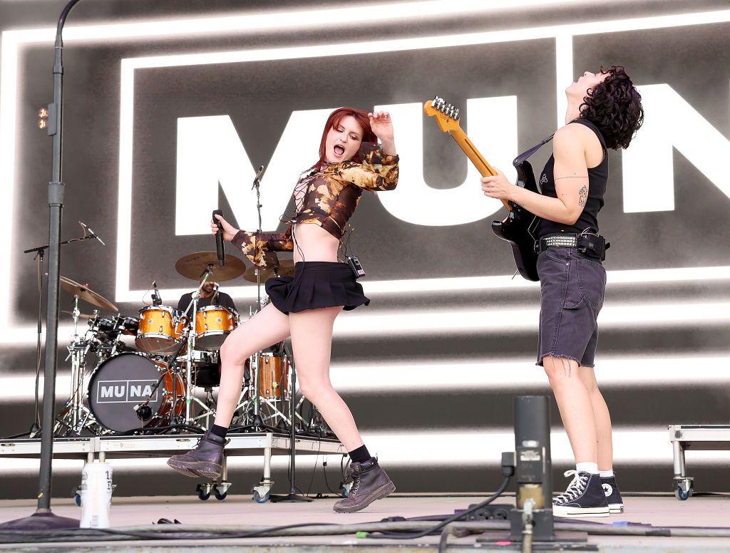 Muna on stage at the Bonnaroo music festival in 2023. Katie is leaping into the air, while Josette throws her head backwards, mid-guitar solo.