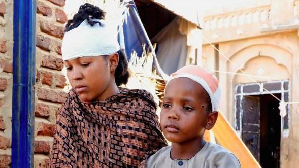 A young woman and a boy, with bandages over their heads, sit in el-Obeid city on 12 January 2026. Both sustained injuries during a drone strike.