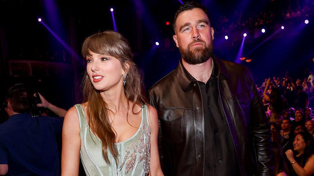 Taylor Swift in a beaded silver dress and Travis Kelce in an all-black ensemble