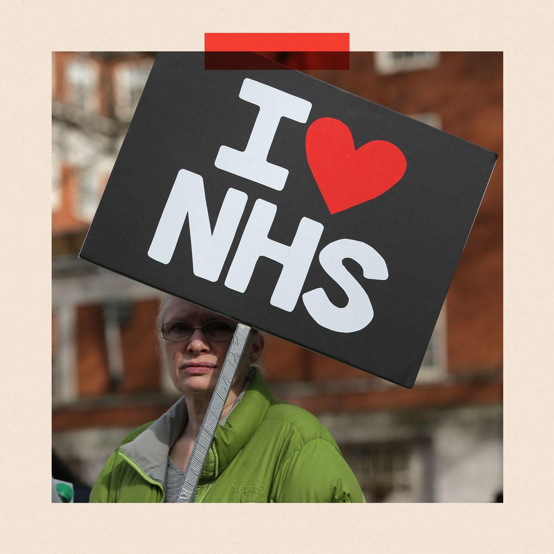 A woman holds a sign which reads I heart NHS