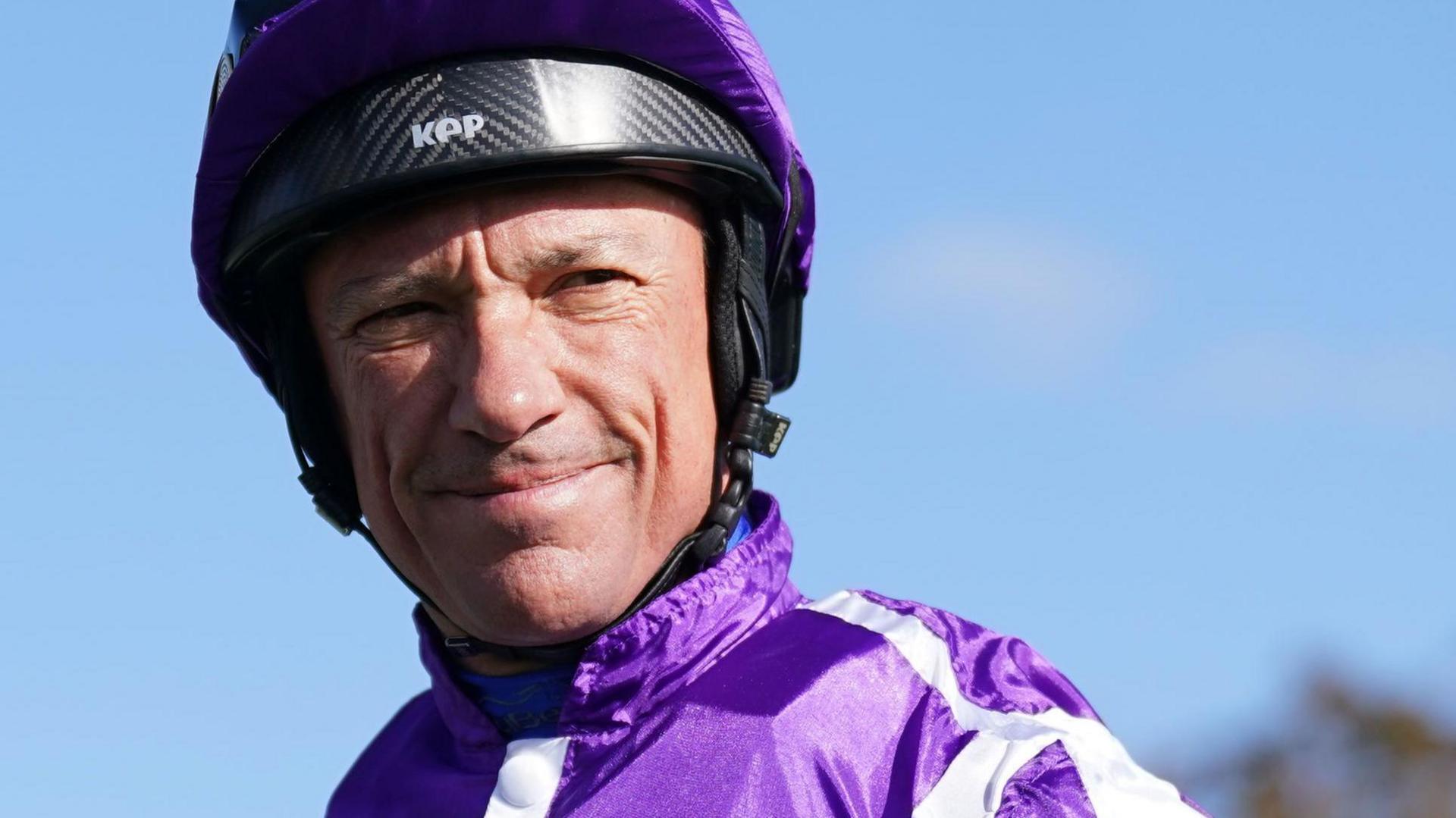 A jockey wearing a blue jacket and helmet with a purple cloth on it.