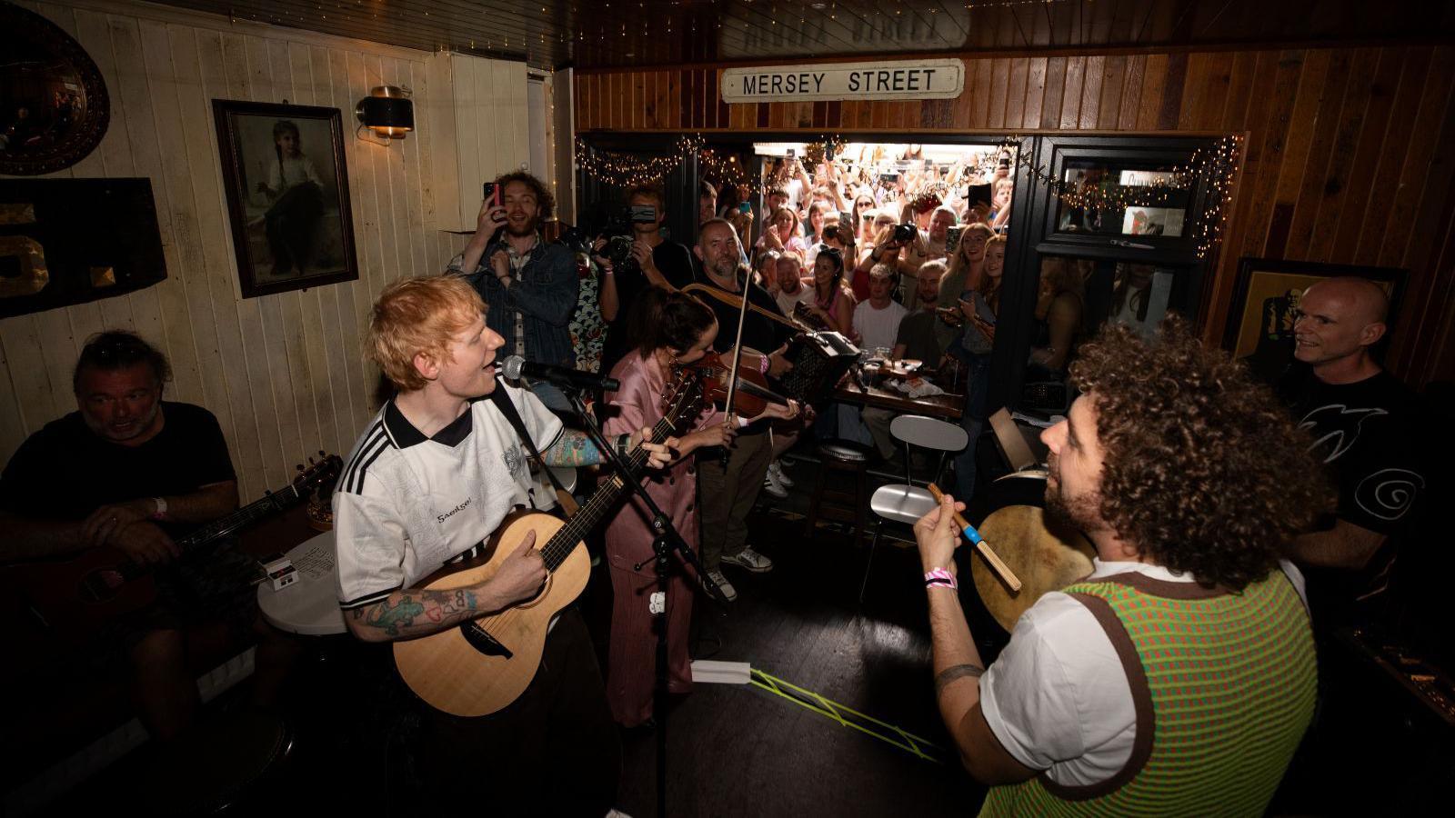 Ed Sheeran singing and playing a guitar in a pub.