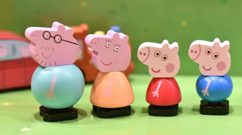 Four wooden figurines of the Peppa Pig family lined up in a row