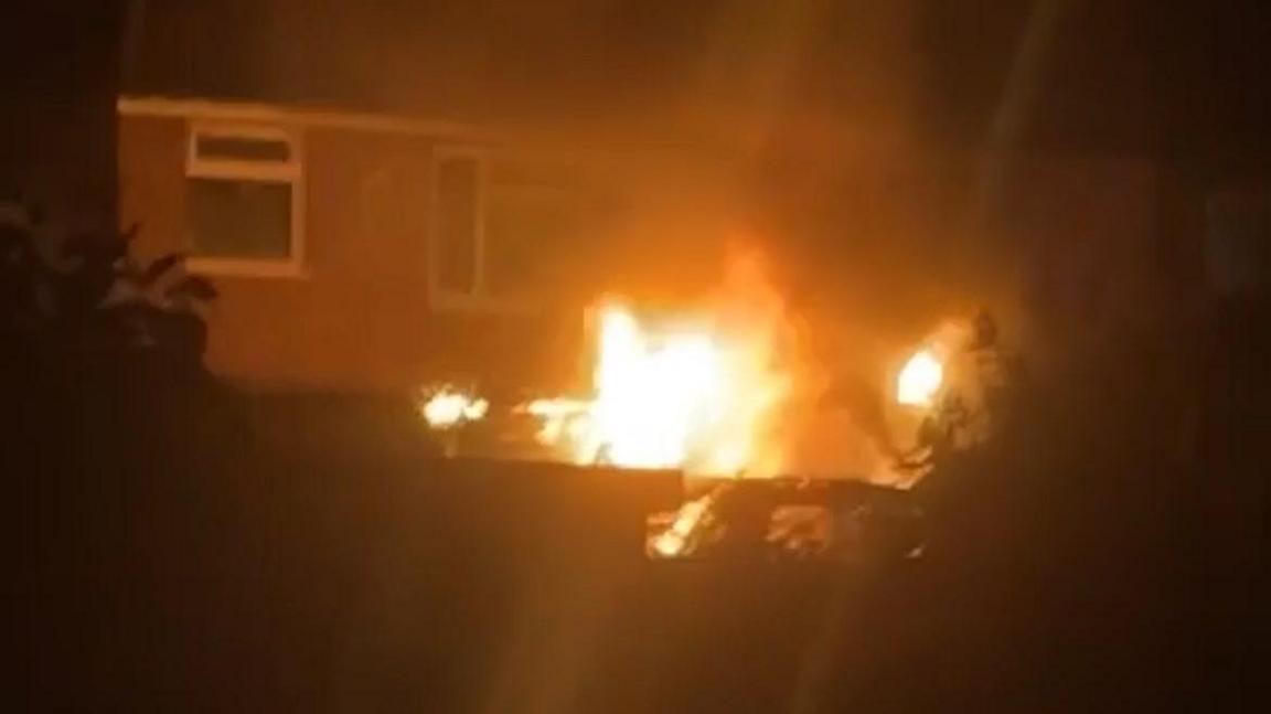 A picture of a house in the dark with orange flames coming from the ground floor