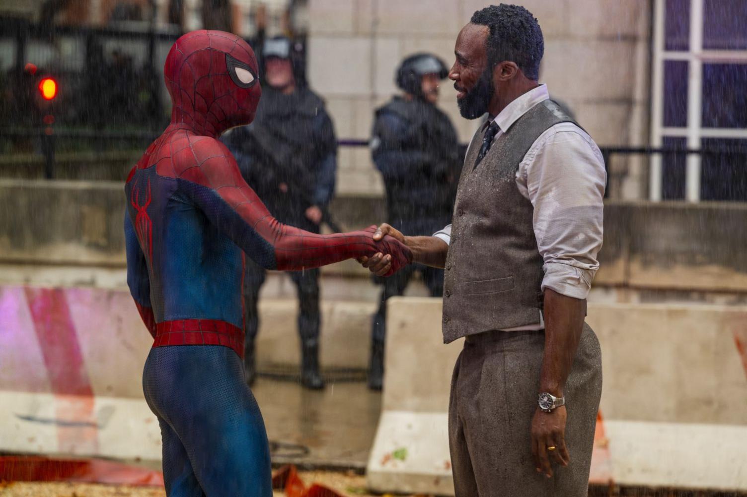 Spiderman shaking hands with a man in a waistcoat, shirt, tie and trousers.