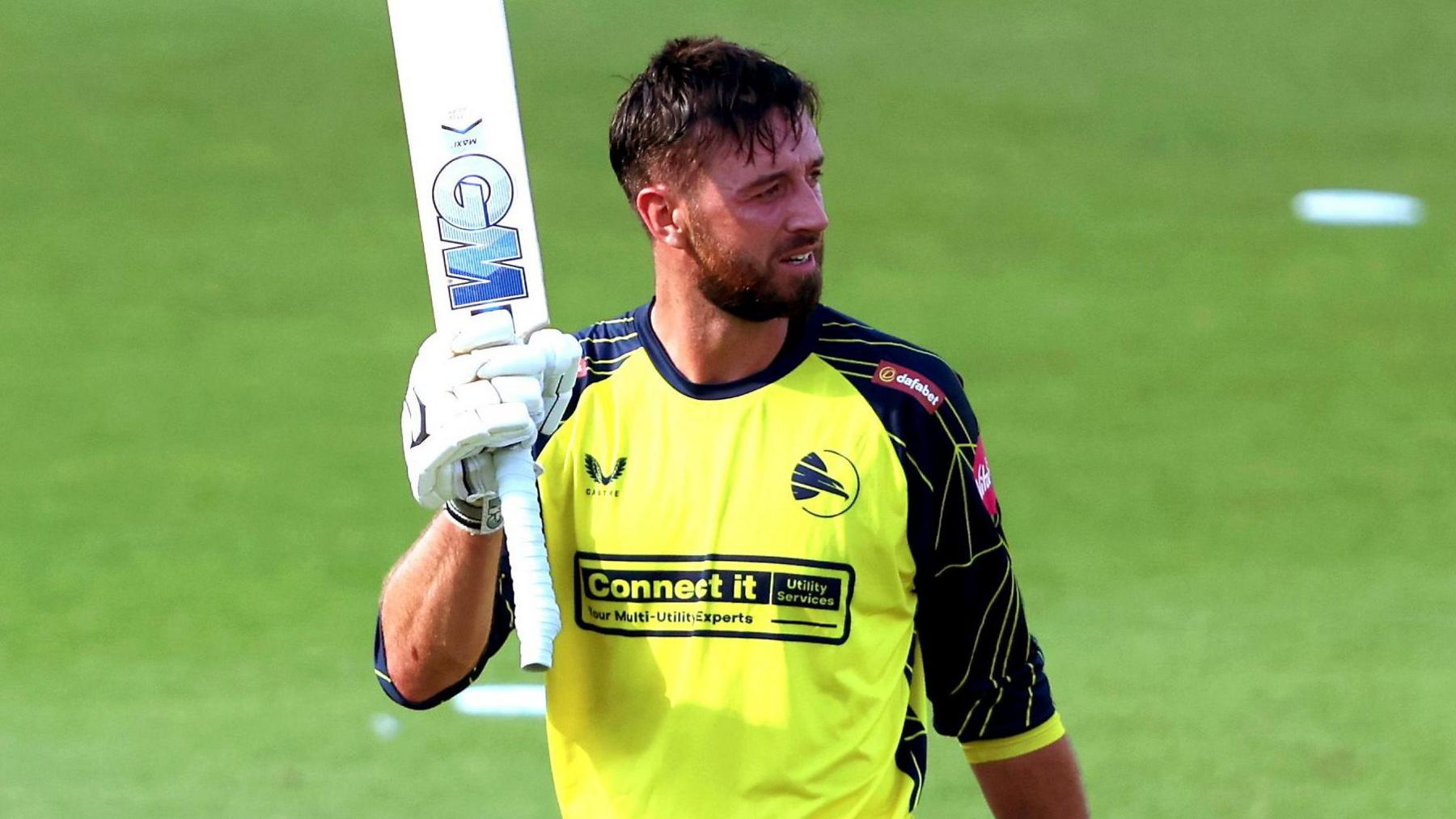 James Vince, wearing Hampshire's bright yellow jersey, raises his bat after getting a century