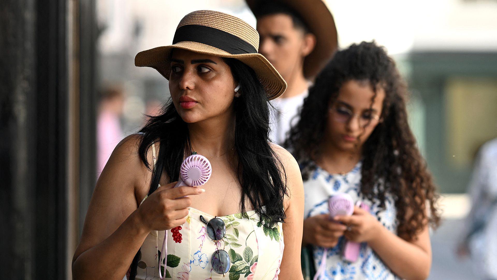 People walk down a street carrying portable electric fans and looking hot, while wearing summer clothing, in York on 24 June.