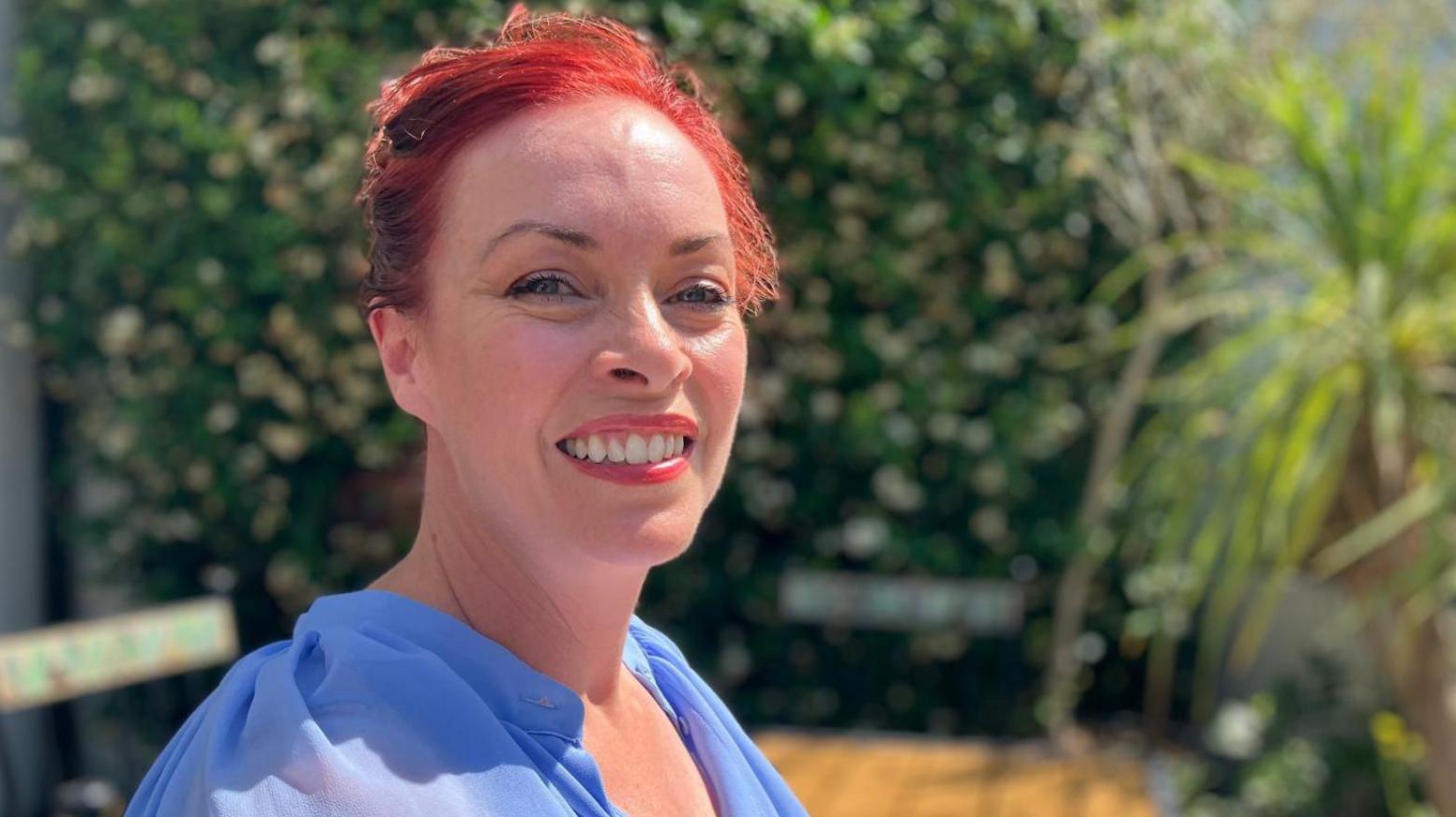 This Morning TV's soap expert Sharon Marshall sits in the sunshine. She is smiling at the camera and is wearing a bright blue blouse.