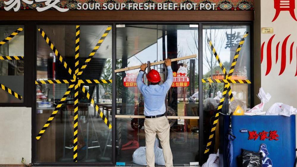 Qi Pengwen, regional manager of the Youth Coast shopping mall, secures the door of a restaurant with wooden bars