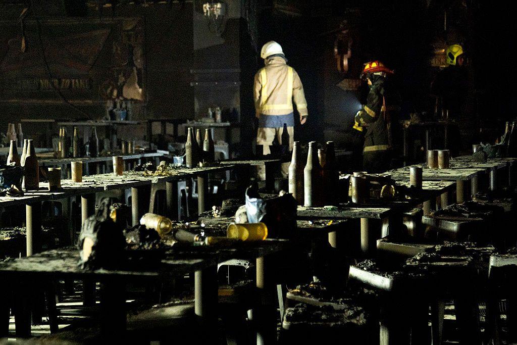 Search and rescue teams inspect the interior of the bar, which is almost entirely charred. Blackened cups, bottles of beer and and beer buckets are seen on the tables
