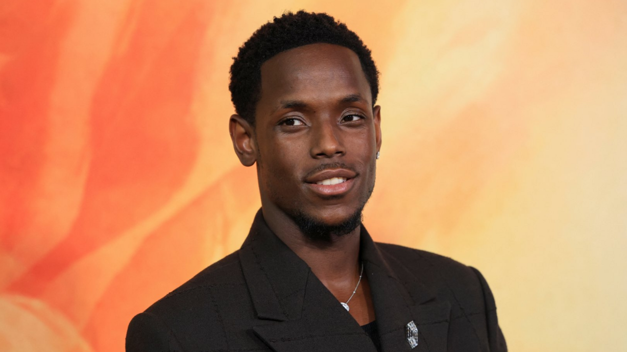 Actor Micheal Ward poses on the red carpet wearing a dark brown suit and black shirt