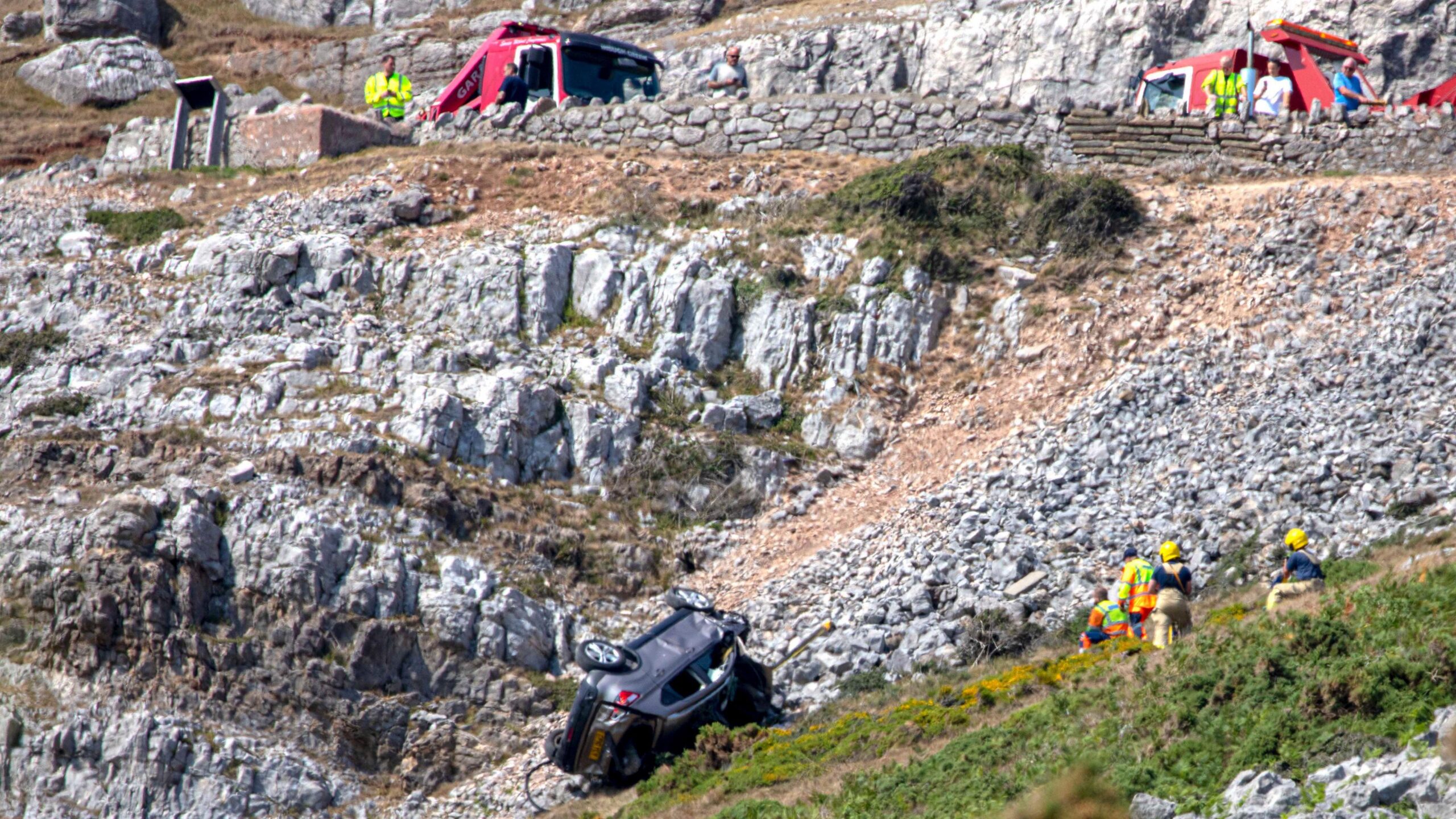 Crews work to recover the vehicle which is lying upside down and pointing back up the slopes