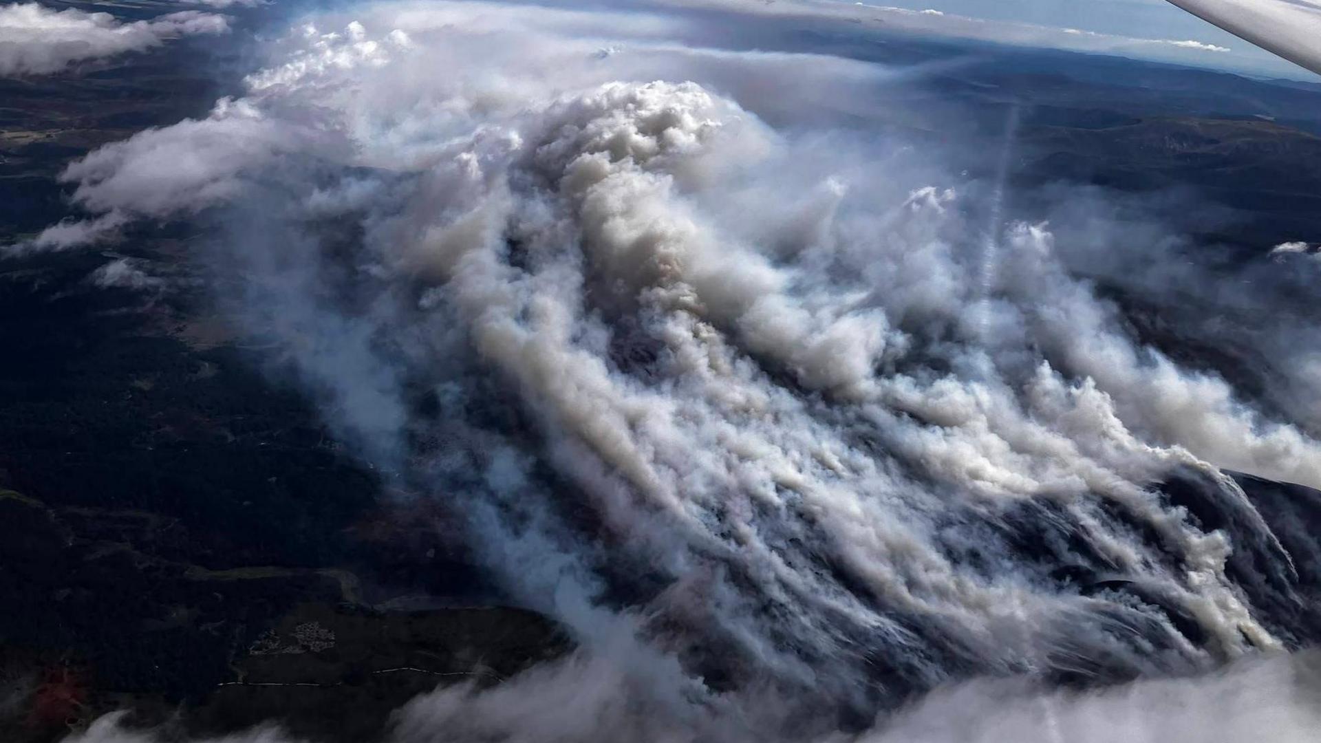 The aerial image shows thick smoke rising from a landscape of hills and moorland.