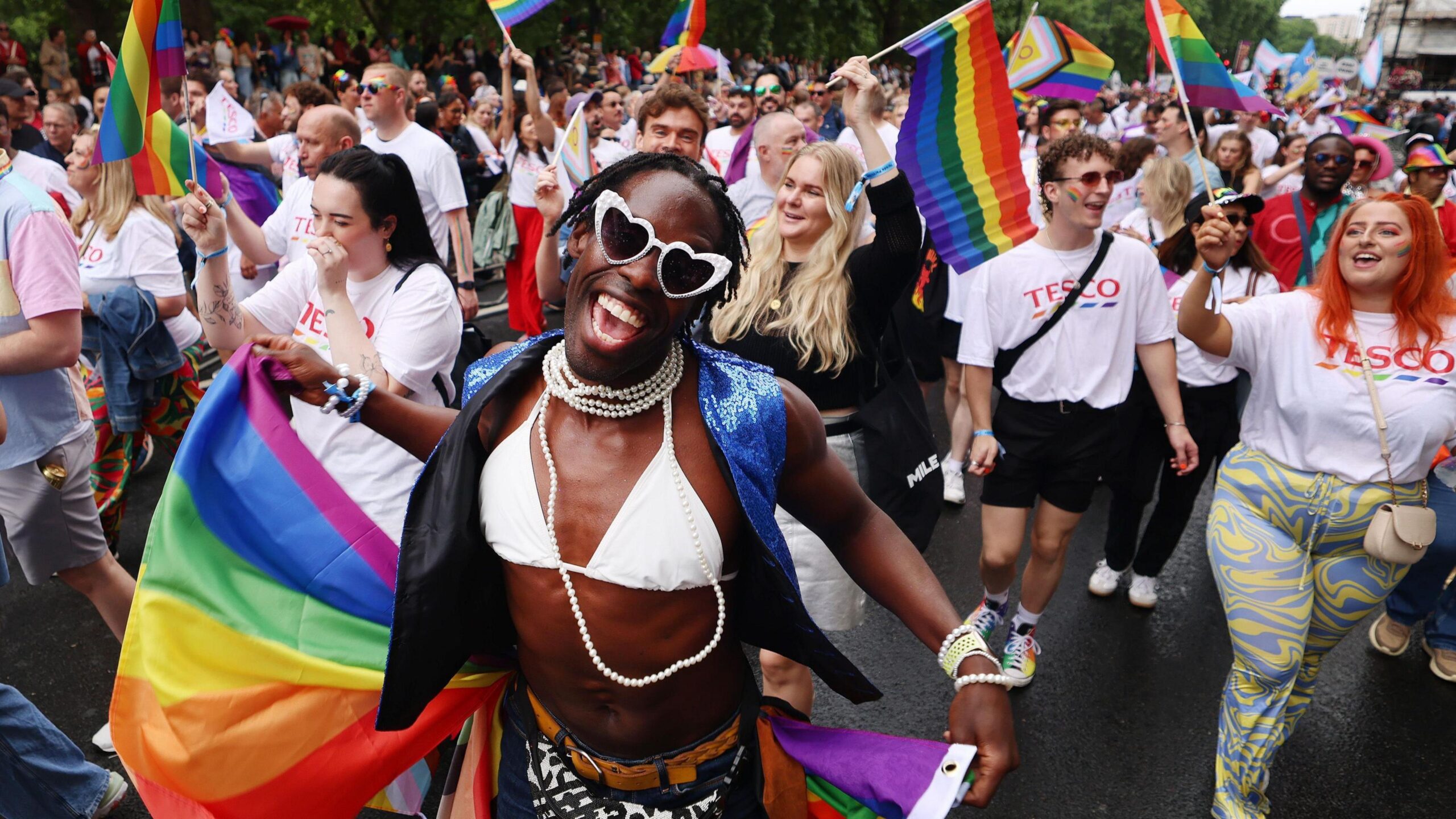 Pride revellers take part in the annual parade in London in 2025. Some people are waving rainbow flags and wearing face paint.