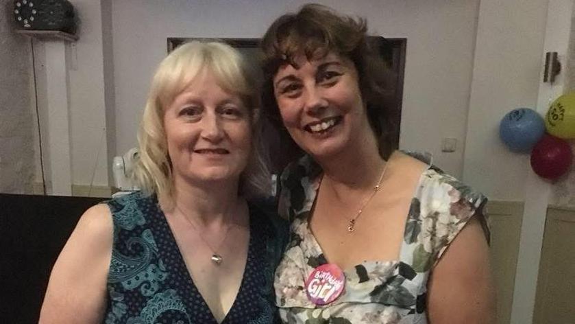 Two women standing close together indoors at what appears to be a celebration.