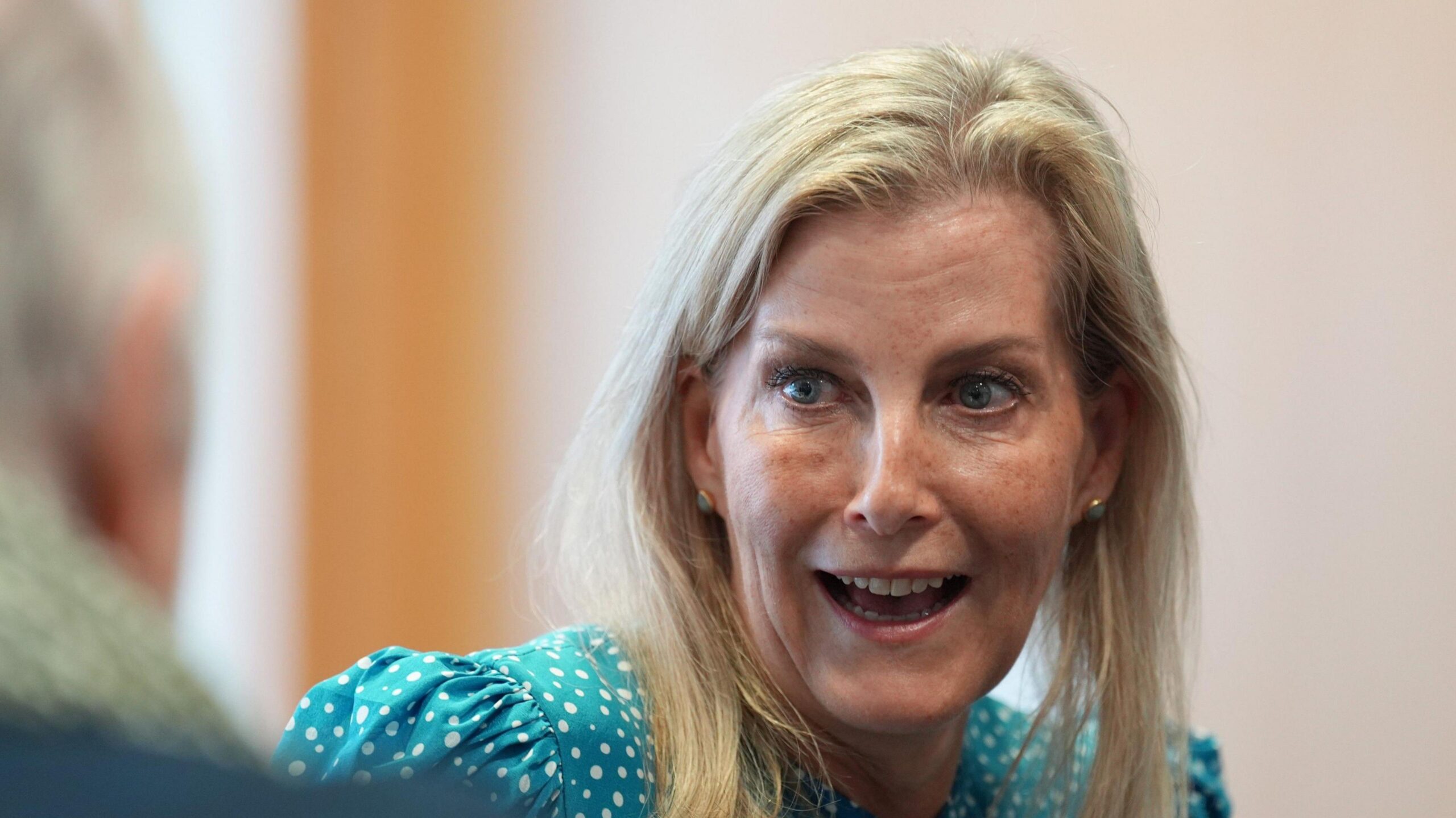 A woman wearing a blue and white polka dot dress smiles while in conversation