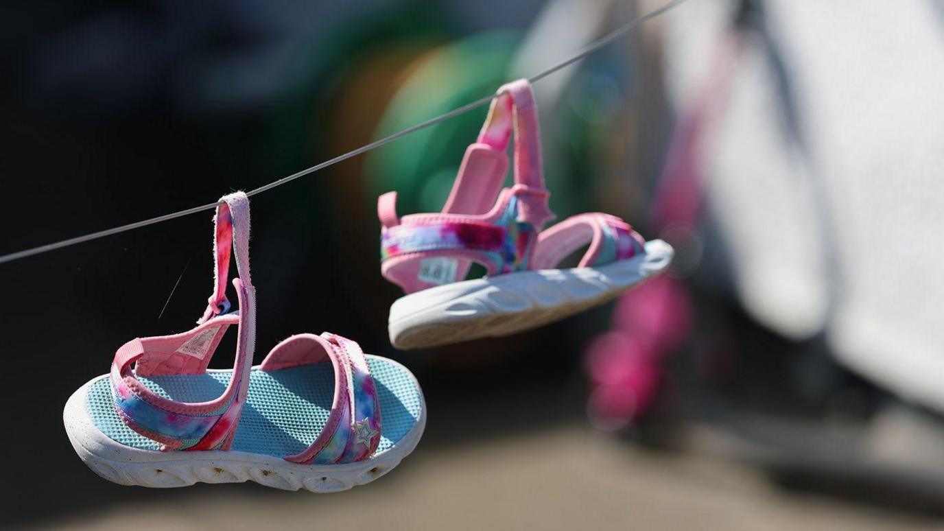 A pair of pink and blue children's sandals hang from a washing line