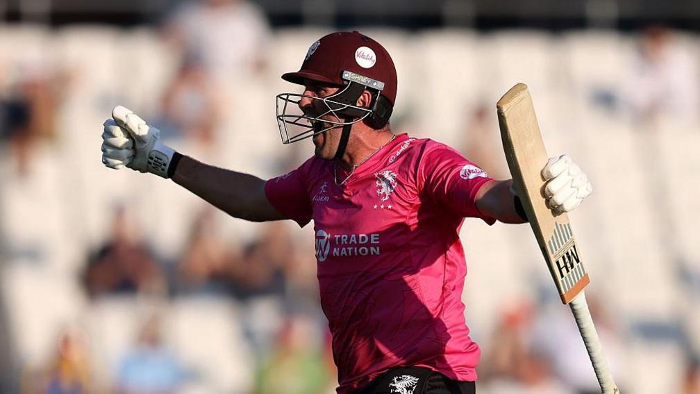 Craig Overton celebrates his match-winning knock against Yorkshire, punching the air and holding his bat wearing the pink shirt and maroon helmet of Somerset