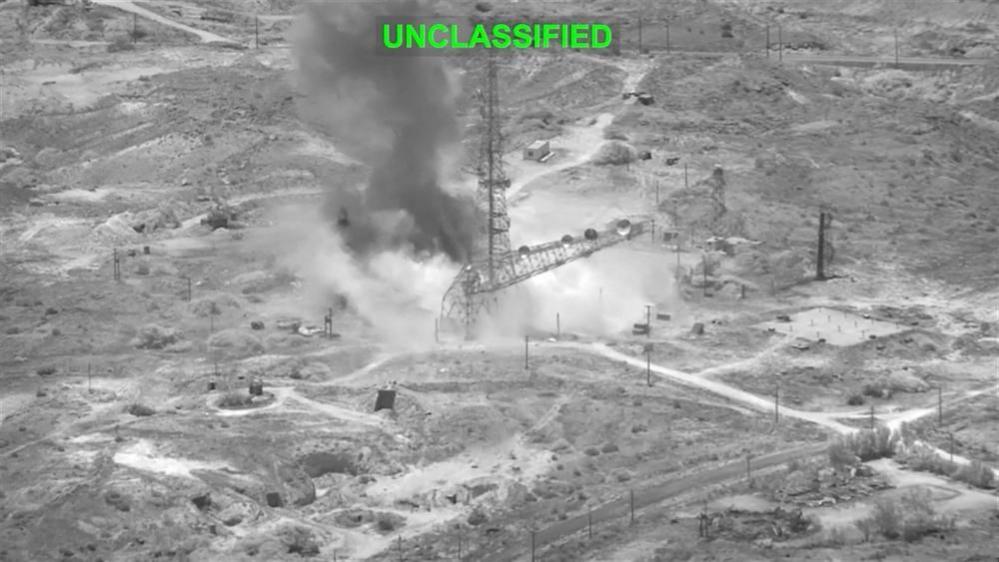 Smoke rises from an explosion at an unknown location, during what U.S. Central Command (CENTCOM) says are strikes on Iran. The image is black and white and there is green text at the top saying 'unclassified'
