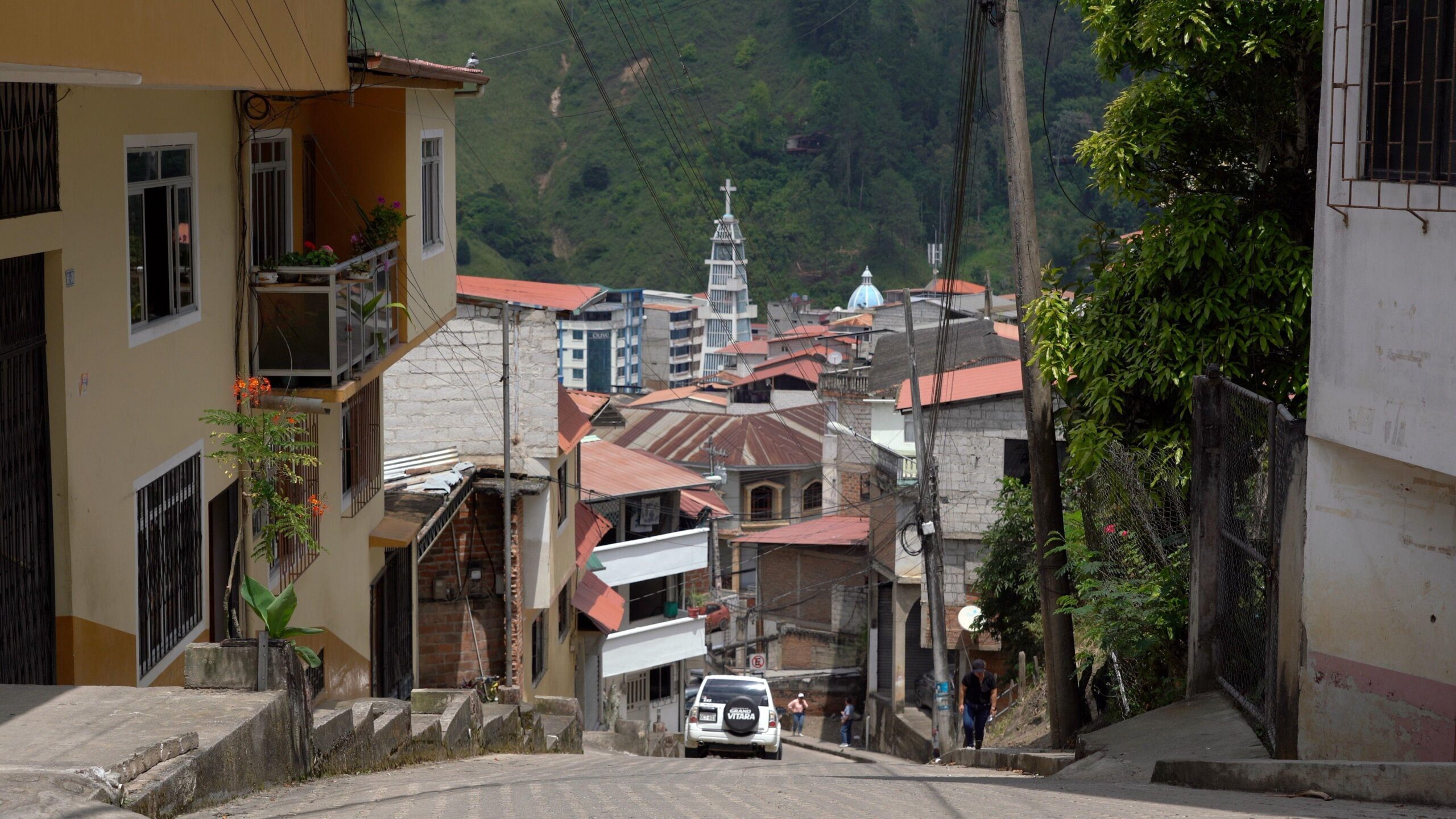 Picture of Piñas, taken from the top of a steep hill, with buildings on each side and the green hillside of a mountain in the distance