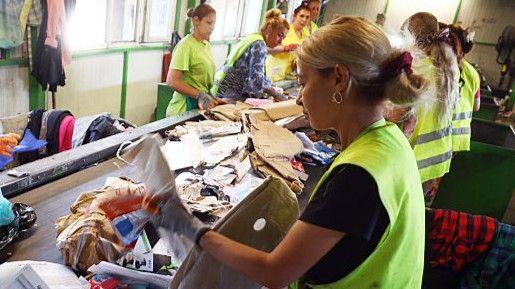 A woman in a high-biz vest sorts paper on a recycling line