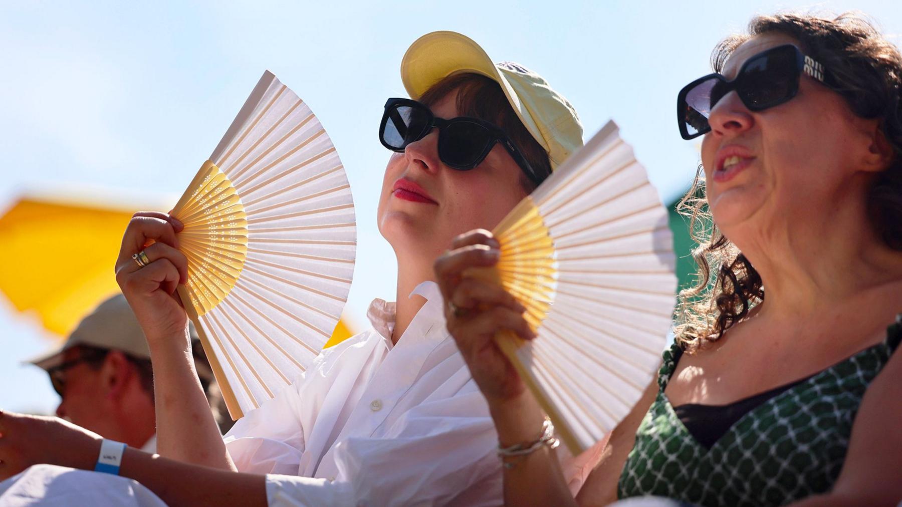 Two women in sunglasses fan themselves, with blue sky and sunshine overhead, while visiting London Zoo on 9 July.